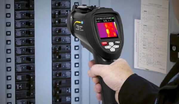 A handheld black thermal imaging camera with a screen displaying a thermal image in various colors. There are several buttons below the screen for controlling the device.