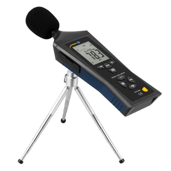 A digital sound level meter on a tripod stand. The device has a rectangular screen displaying a reading of 18.3 decibels and control buttons on the front. The sensor on top is covered with a black windscreen. The tripod legs are adjustable and silver in color.